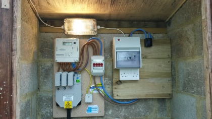 A supply board in an outbuilding with meter, consumer unit and sockets on a timber backboard