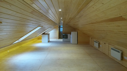 A long pine-clad loft room with lights in the ceiling and heaters along the wall