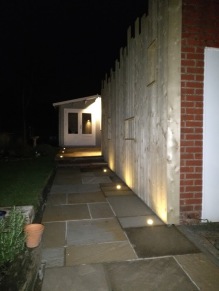 A garden path at night lit by small lights set along a timber fence